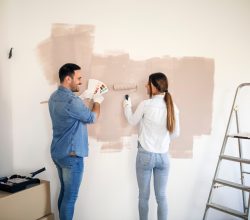 Para maluje ścianę używając jasnej farby do wnętrz
