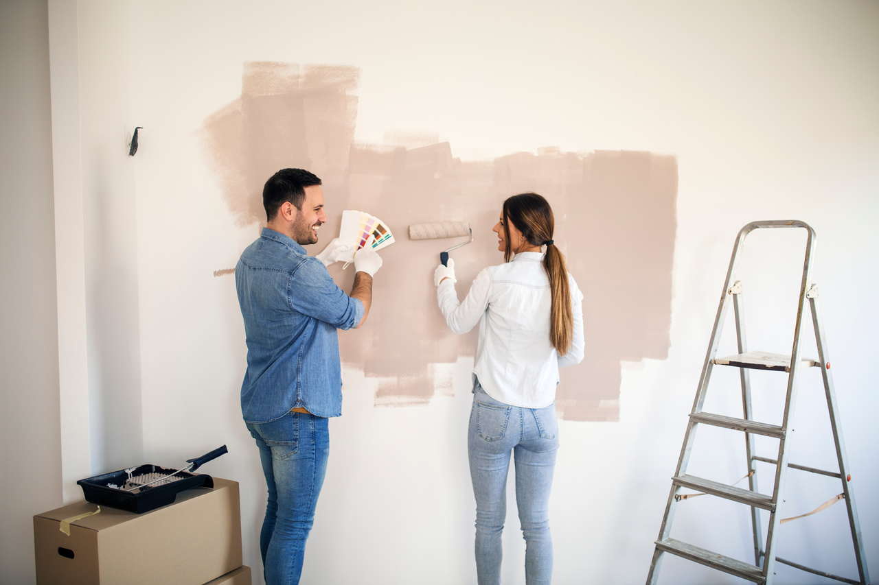 Para maluje ścianę używając jasnej farby do wnętrz